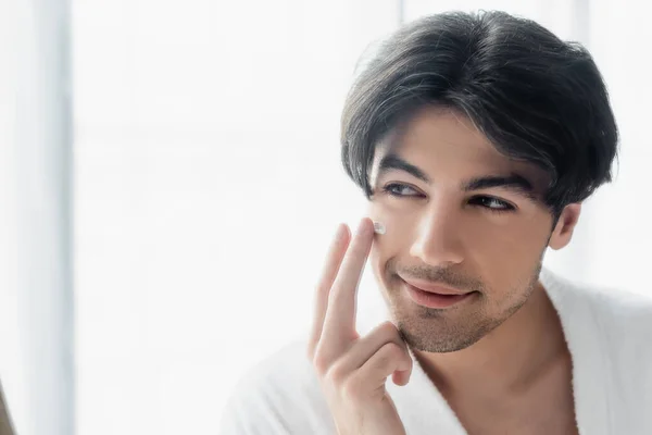 Uomo bruna sorridente applicare la crema per il viso in bagno — Foto stock