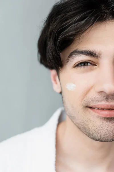 Vista de cerca del hombre recortado con crema cosmética en la cara aislado en gris - foto de stock