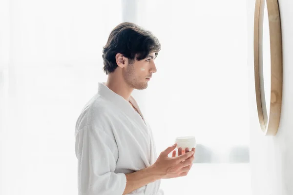 Vue latérale de l'homme avec crème visage regardant dans le miroir dans la salle de bain — Photo de stock