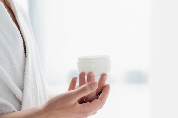 Cropped view of man in bathrobe holding container with cosmetic cream — Stock Photo