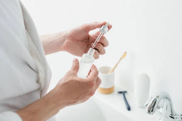 Vue recadrée de l'homme tenant bouteille avec sérum cosmétique dans la salle de bain — Photo de stock