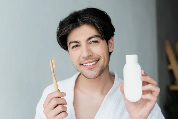 Happy brunette man holding toothbrush and toothpaste while looking at camera — Stock Photo