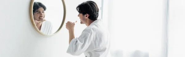 Feliz joven mirando en el espejo mientras se cepilla los dientes en el baño, pancarta - foto de stock