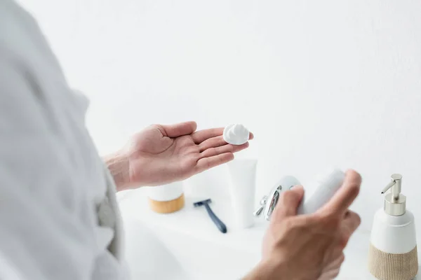 Cropped view of man holding shaving foam near blurred toiletries and safety razor — Stock Photo