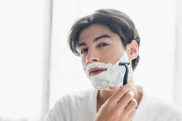 Brunette man looking at camera while shaving with safety razor — Stock Photo