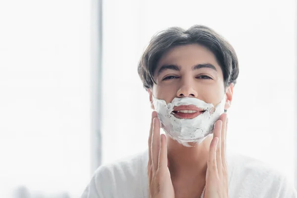 Pleased man looking at camera while applying shaving foam in bathroom — Stock Photo