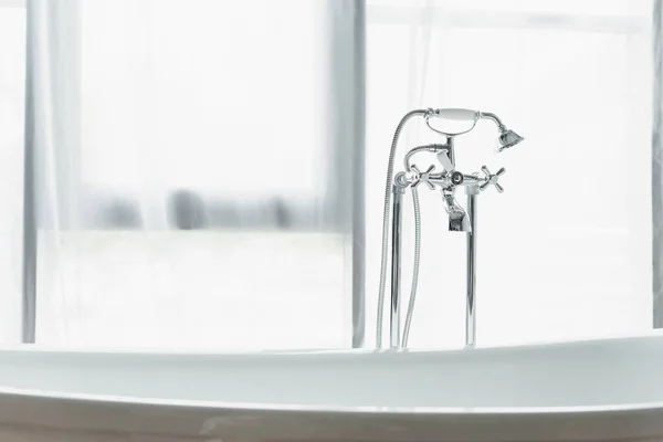 Metallarmatur mit Duschkopf, weiße Badewanne neben weißem Vorhang im Badezimmer — Stockfoto