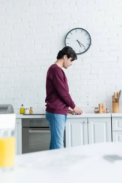 Giovane in piedi in cucina vicino a tazza di caffè, primo piano sfocato — Foto stock