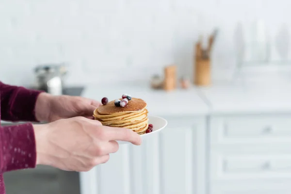 Vista parcial del hombre sosteniendo deliciosos panqueques con arándanos en cocina borrosa - foto de stock