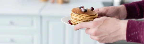 Vista recortada del hombre sosteniendo deliciosos panqueques con arándanos frescos, pancarta - foto de stock