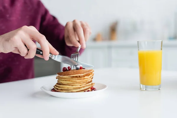 Partial view of man cutting pancakes near glass of orange juice — Stock Photo