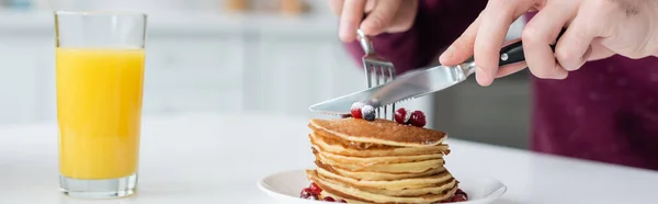 Vista ritagliata di uomo che taglia frittelle vicino a vetro di succo d'arancia fresco, banner — Foto stock