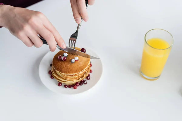 Vista superior do homem cortado cortando panquecas saborosas perto de vidro de suco de laranja fresco — Fotografia de Stock