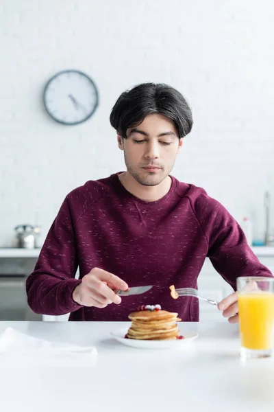 Brunette man eating tasty pancakes near blurred glass of orange juice — Stock Photo