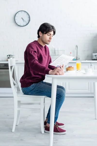 Visão de comprimento total do homem ler jornal da manhã perto do café da manhã na mesa da cozinha — Fotografia de Stock