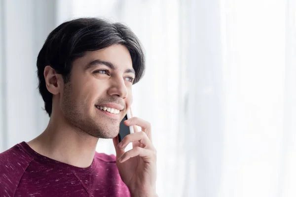 Jovem morena homem sorrindo durante conversa telefônica em casa — Fotografia de Stock