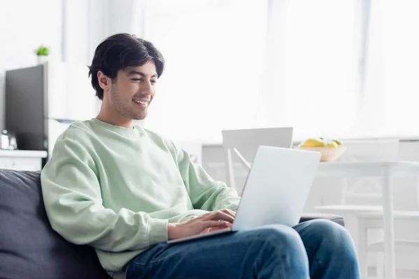 Homem satisfeito usando laptop enquanto sentado no sofá em casa — Fotografia de Stock