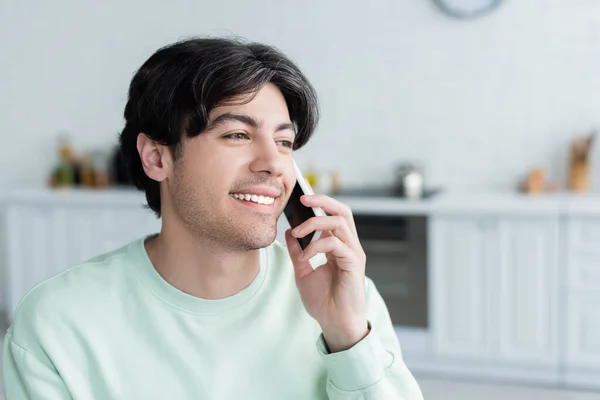 Glücklicher junger Mann spricht in verschwommener Küche auf Smartphone — Stockfoto