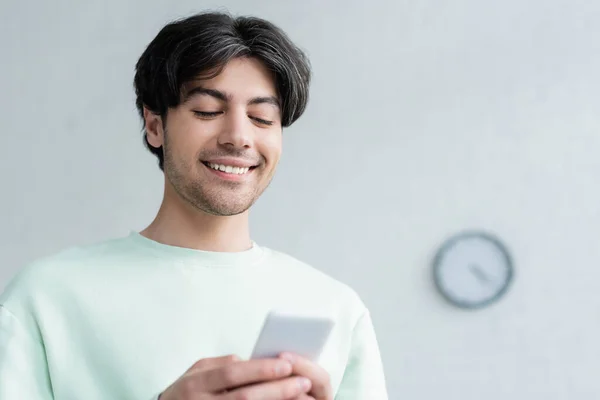 Glücklich brünette Mann chattet auf verschwommenem Handy zu Hause — Stockfoto