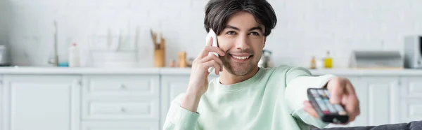 Uomo sorridente cliccando canali tv mentre parla su smartphone a casa, banner — Foto stock