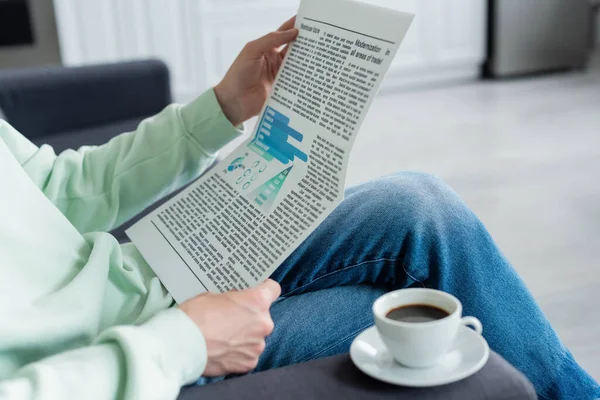 Cropped view of man reading newspaper near coffee cup on sofa — Stock Photo