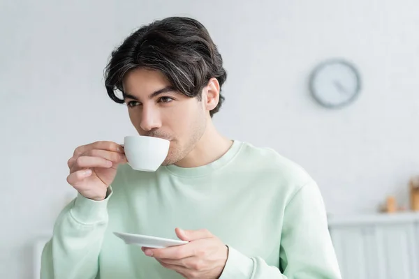 Jovem morena homem segurando pires enquanto bebe café da manhã — Fotografia de Stock