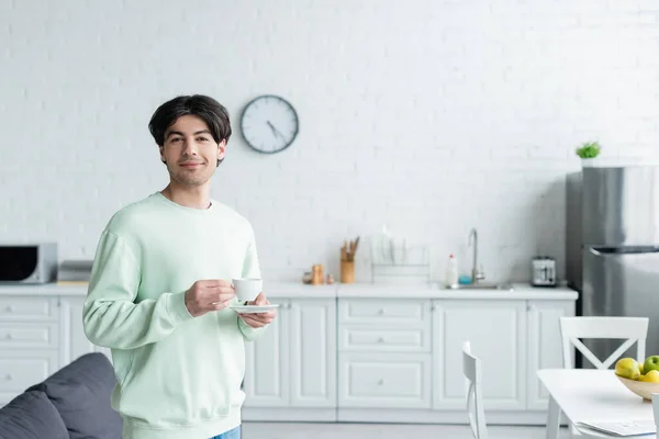 Lächelnder brünetter Mann mit Kaffeetasse blickt in moderne Küche in die Kamera — Stockfoto