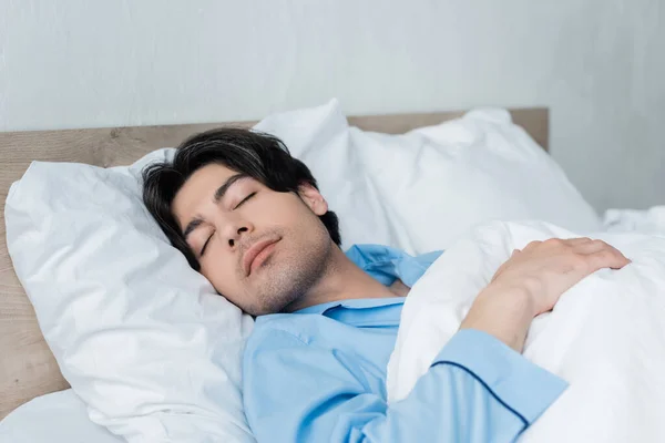 Homem morena em pijama azul dormindo em roupa de cama branca de manhã — Fotografia de Stock