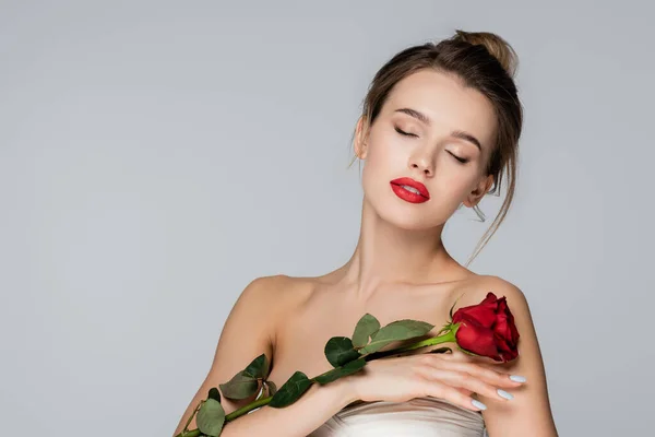 Jeune femme avec maquillage et les yeux fermés posant avec rose rouge isolé sur gris — Photo de stock