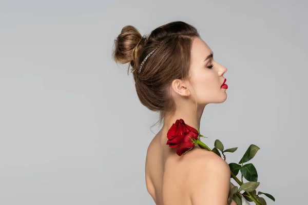 Вид сбоку молодой женщины с красной розой на голом плече, изолированной на сером — стоковое фото