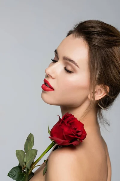 Mujer sensual con los ojos cerrados posando cerca de rosa roja aislada en gris - foto de stock