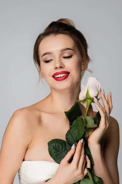 Femme souriante aux épaules nues tenant rose blanche isolée sur gris — Photo de stock