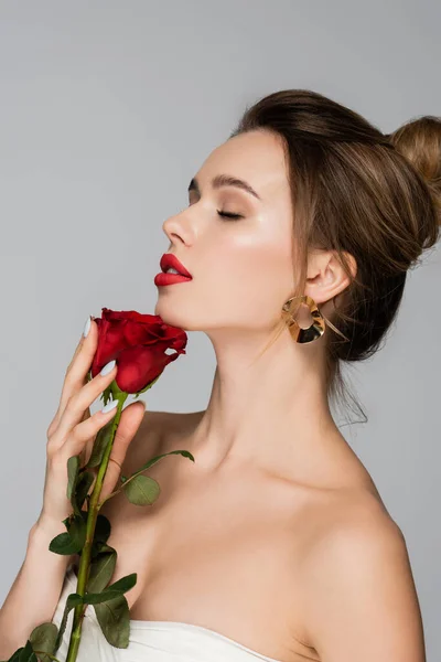 Encantadora mujer con hombros desnudos y labios rojos sosteniendo rosa aislado en gris - foto de stock