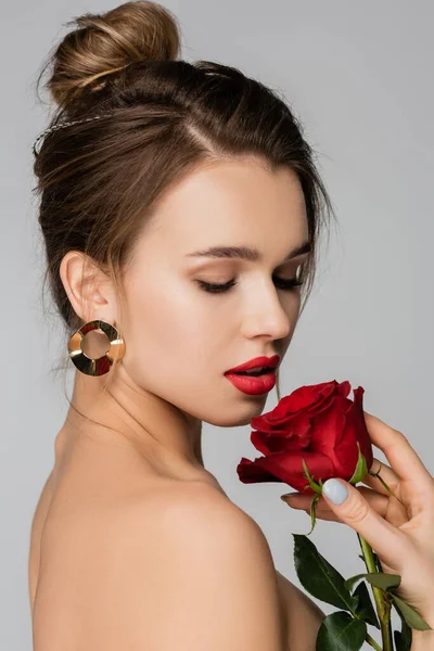 Pretty woman in golden earring holding red rose isolated on grey — Stock Photo