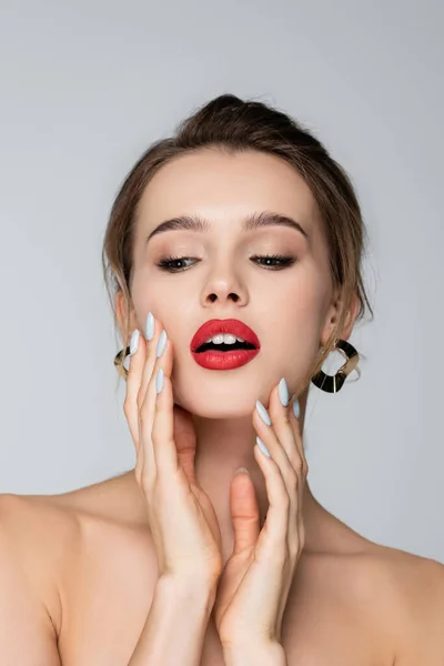 Sensual joven con labios rojos tocando la cara aislada en gris — Stock Photo