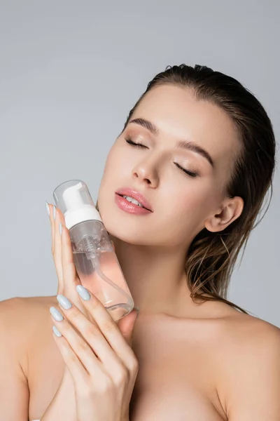 Mujer sensual con los ojos cerrados que sostiene la espuma cosmética cerca de la cara aislada en gris — Stock Photo