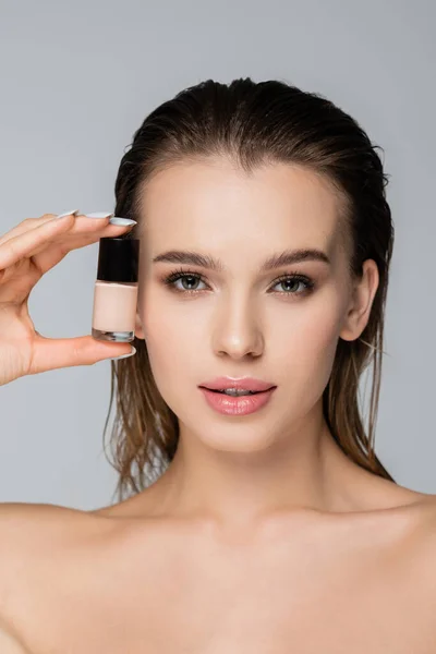 Young woman with natural makeup holding face foundation isolated on grey — Stock Photo