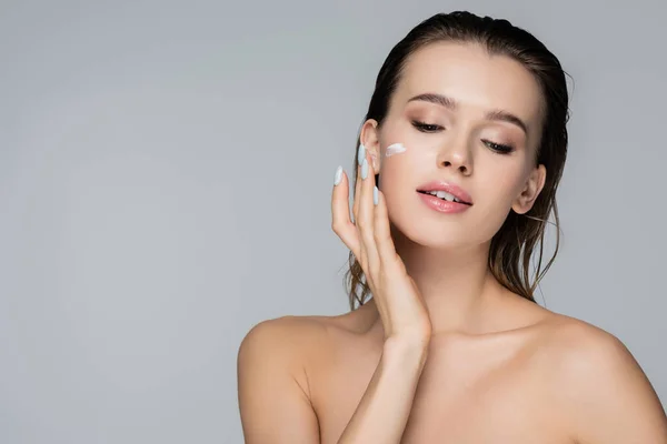 Young woman with bare shoulders applying face cream isolated on grey — Stock Photo