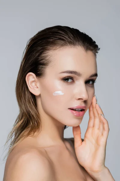 Mujer joven con crema cosmética en la cara perfecta mirando a la cámara aislada en gris - foto de stock