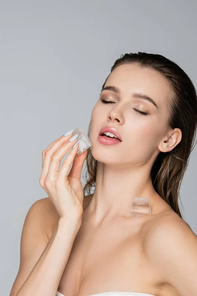 Young and sensual woman with wet hair and ice cubes posing isolated on grey — Stock Photo