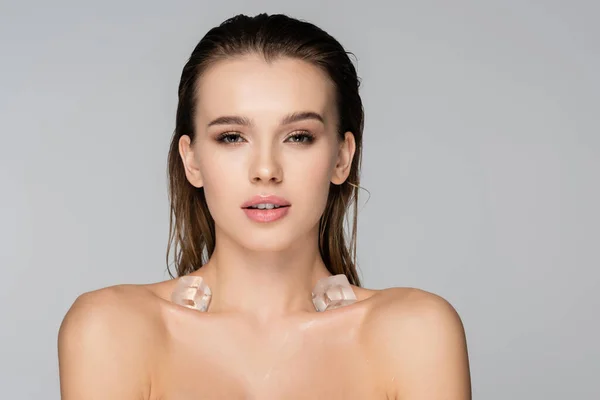 Young and sensual woman with ice cubes on bare shoulders isolated on grey — Stock Photo