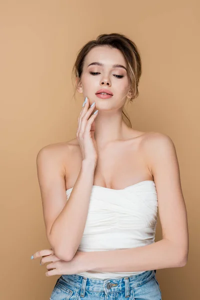 Young and charming woman in strapless top touching face isolated on beige — Stock Photo