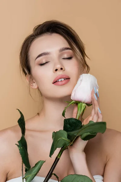 Giovane e sensuale donna ad occhi chiusi toccando rosa bianca isolata sul beige — Foto stock