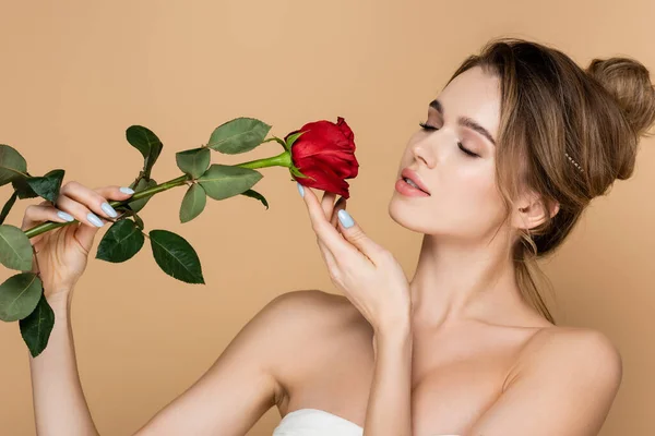 Mulher sensual com olhos fechados e ombros nus posando com rosa vermelha isolada no bege — Fotografia de Stock