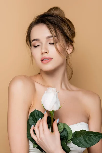 Charming woman with closed eyes and perfect skin holding white rose isolated on beige — Stock Photo