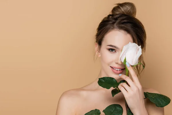 Heureuse jeune femme tenant rose blanche près du visage isolé sur beige — Photo de stock