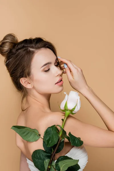 Mujer joven y bonita con los ojos cerrados posando cerca de rosa blanca aislada en beige - foto de stock