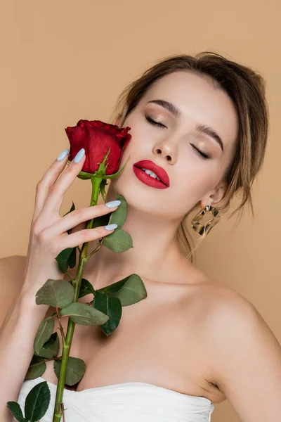 Pretty woman in strapless top holding rose near face with red lips isolated on beige — Stock Photo