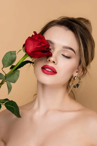 Femme sensuelle avec des lèvres rouges tenant rose fraîche près du visage isolé sur beige — Photo de stock