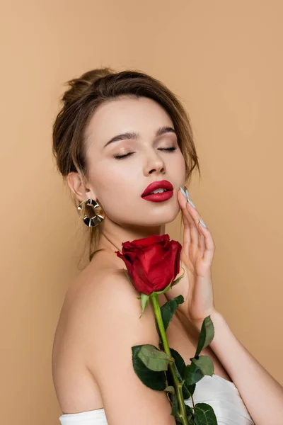 Pretty woman with red rose touching perfect face isolated on beige — Stock Photo